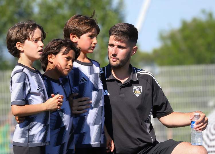Un entraîneur barbu avec trois jeunes joueurs de football, tous regardant dans la même direction.