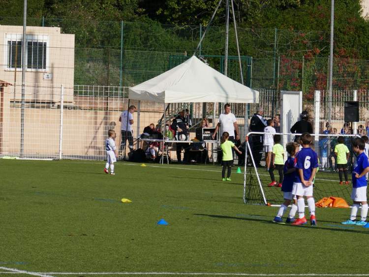 Des jeunes joueurs de football s'entraînent sur un terrain synthétique sous le regard d'adultes.