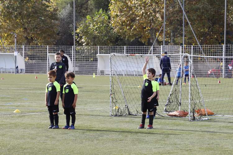 De jeunes footballeurs en maillots noirs et verts s'entraînent sur un terrain de football, avec des adultes en arrière-plan.