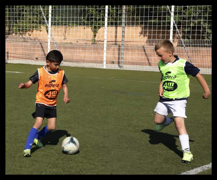 Deux jeunes joueurs de football en chasubles s'entraînent sur un terrain en gazon synthétique.