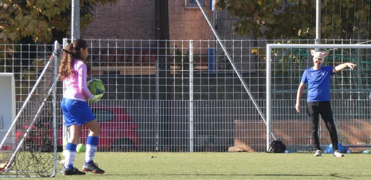 Une gardienne de but avec un ballon et un joueur masqué devant un but de football.