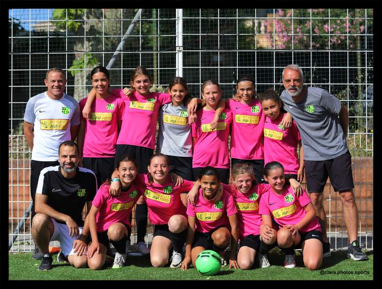 Une équipe de jeunes joueuses de football pose avec leurs entraîneurs sur un terrain ensoleillé.