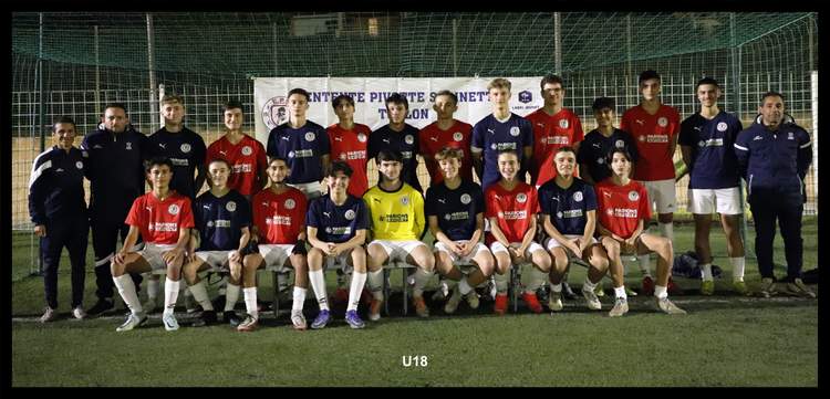 Une équipe de football amateur pose pour une photo de groupe sur le terrain, avec des joueurs et des entraîneurs.
