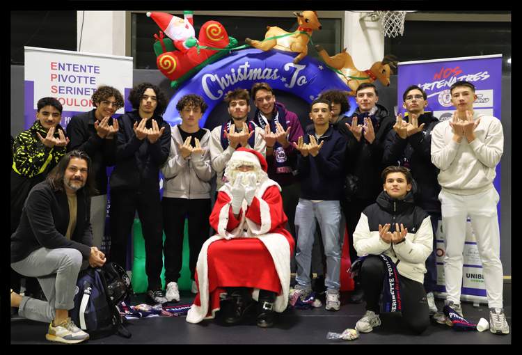 Un groupe de jeunes hommes et un adulte posent avec le Père Noël devant une arche décorative de Noël.