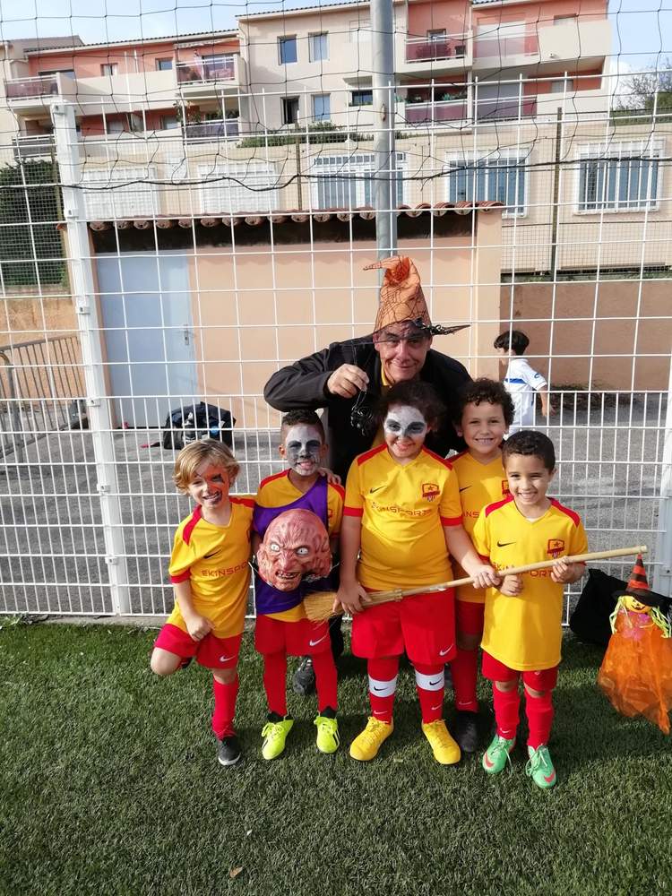 Un groupe d'enfants déguisés pour Halloween posent avec un adulte sur un terrain de football.