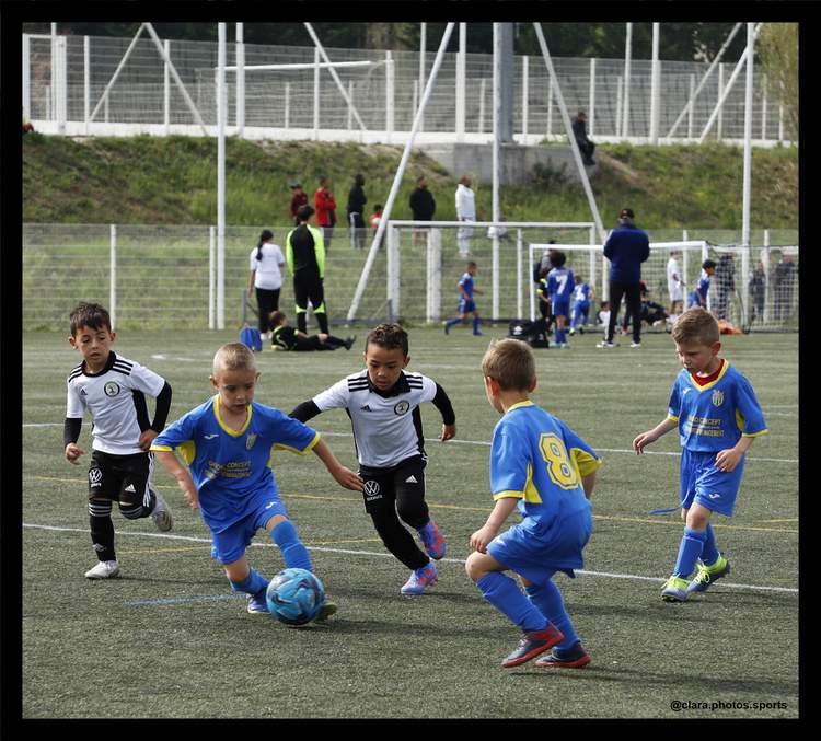Des jeunes joueurs de football en pleine action sur le terrain, avec d'autres personnes en arrière-plan.