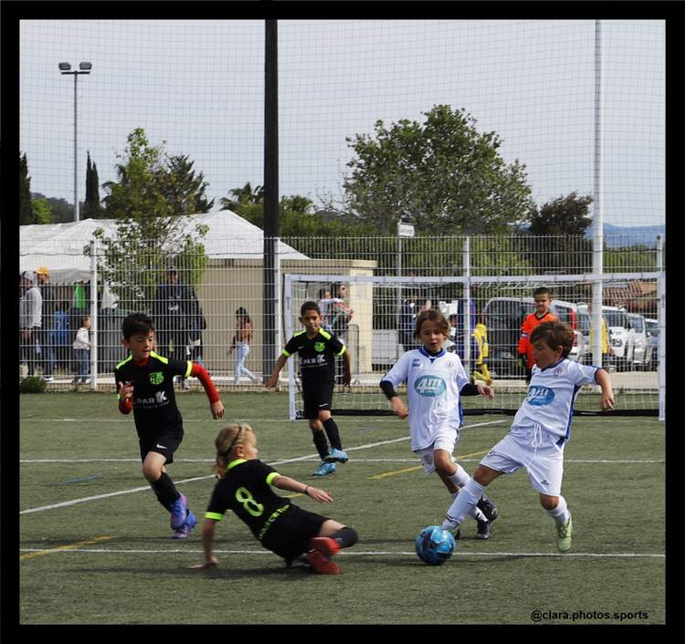 Des jeunes joueurs de football en pleine action sur le terrain, avec un joueur au sol et d'autres autour du ballon.