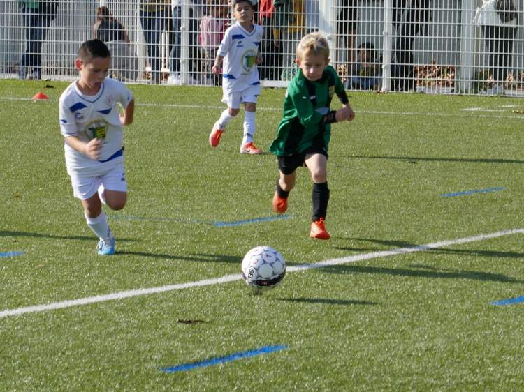 Trois jeunes joueurs de football en pleine action sur un terrain synthétique, un ballon au premier plan.