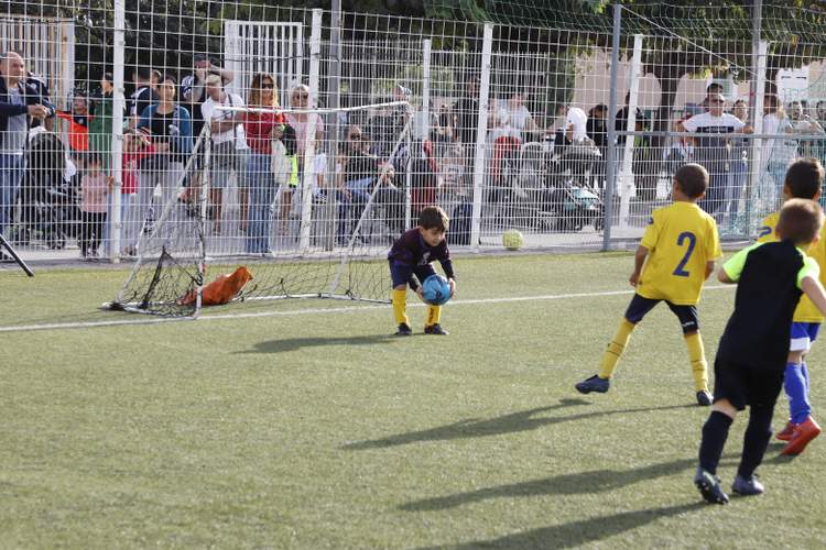 Des jeunes joueurs de football sur un terrain synthétique avec des spectateurs derrière une clôture.