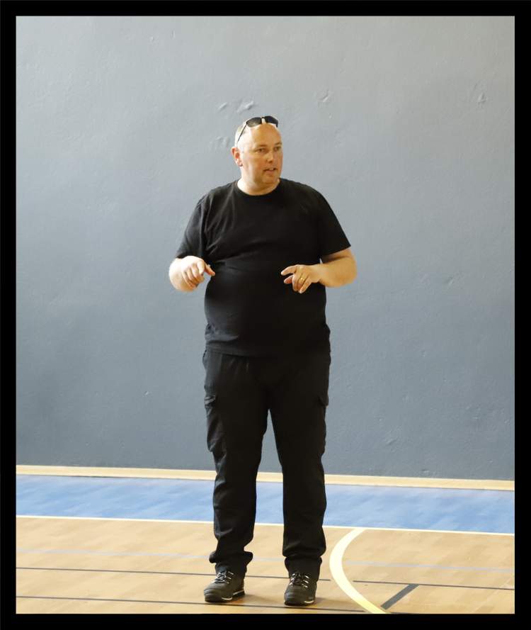 Un homme en tenue décontractée se tient debout sur un terrain de sport en intérieur.