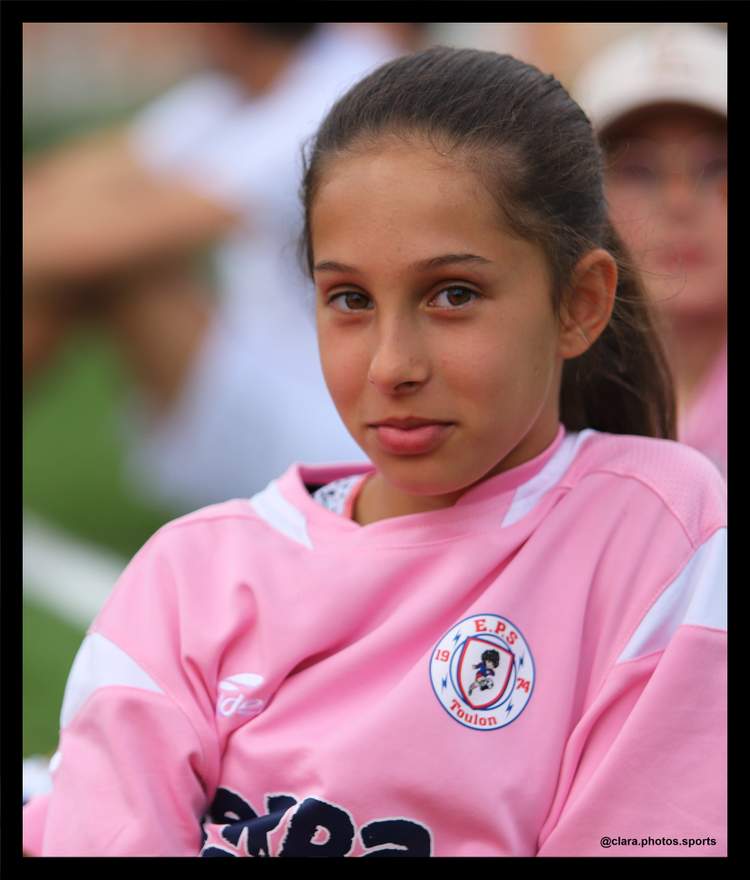 Une jeune fille en maillot de football rose regarde l'objectif avec un léger sourire.