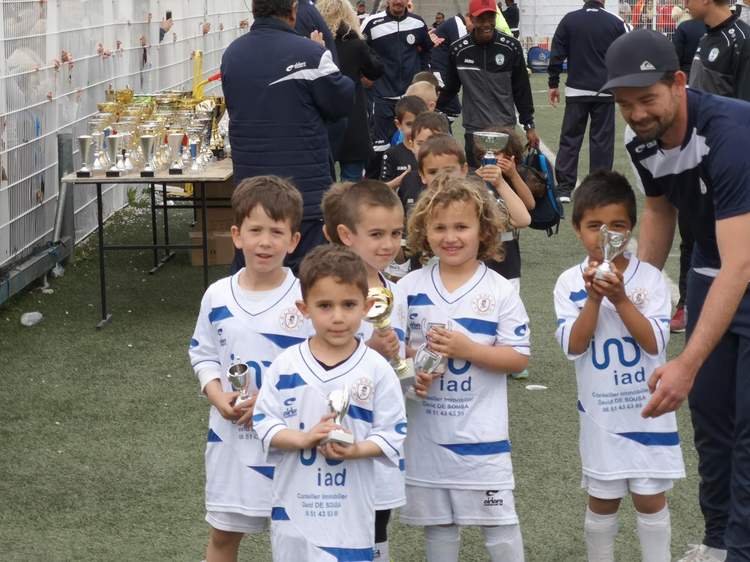 Des jeunes joueurs de football posent avec leurs trophées après un match, entourés d'adultes.