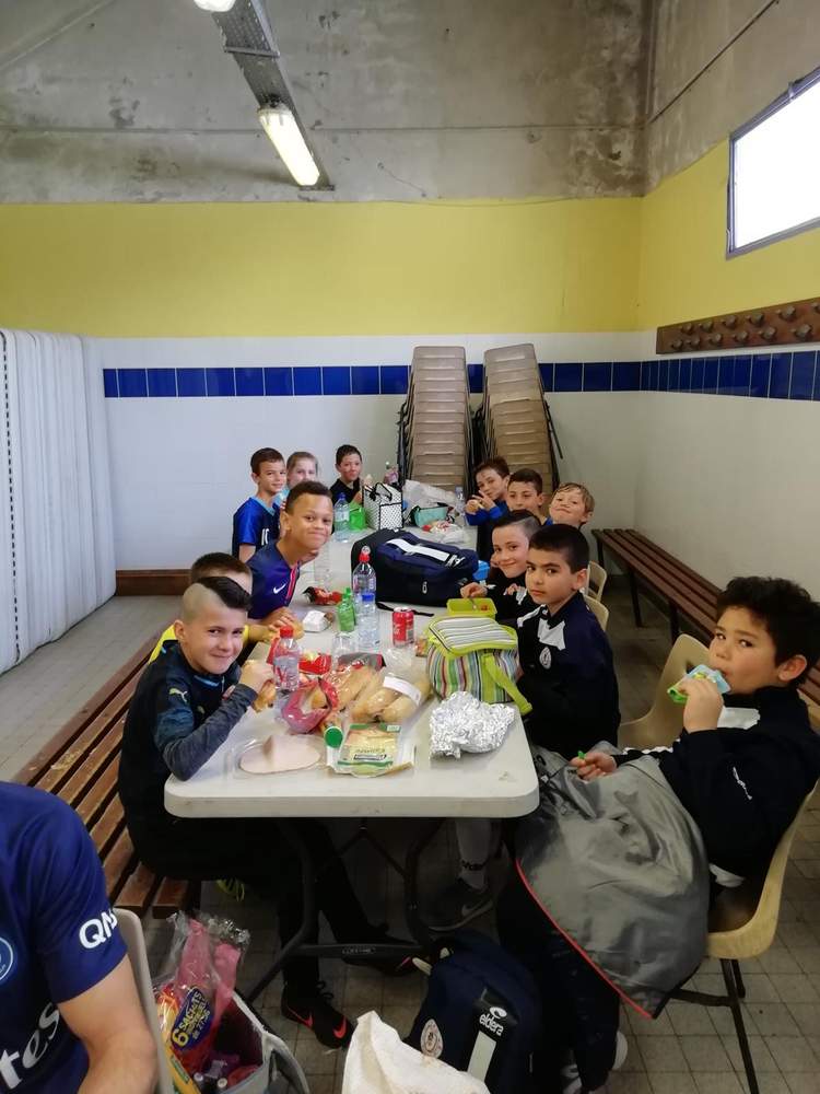 Des jeunes footballeurs partagent un repas autour d'une table dans un vestiaire ou une salle de club.