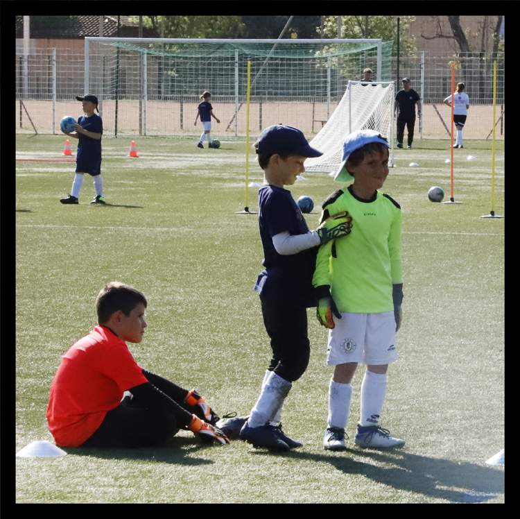 Des jeunes footballeurs s'entraînent sur un terrain synthétique sous le soleil.
