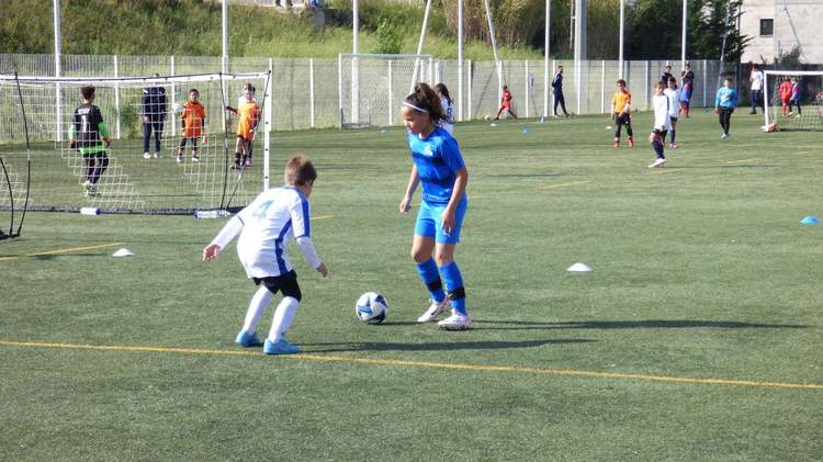 Des jeunes joueurs de football s'entraînent sur un terrain en gazon synthétique sous un ciel ensoleillé.