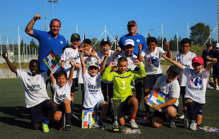 Une équipe de jeunes footballeurs et leurs entraîneurs célèbrent une victoire avec des trophées et des sourires.