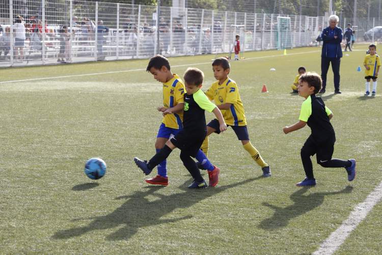 Des jeunes joueurs de football en maillots jaunes et noirs s'affrontent pour le ballon sur un terrain ensoleillé.