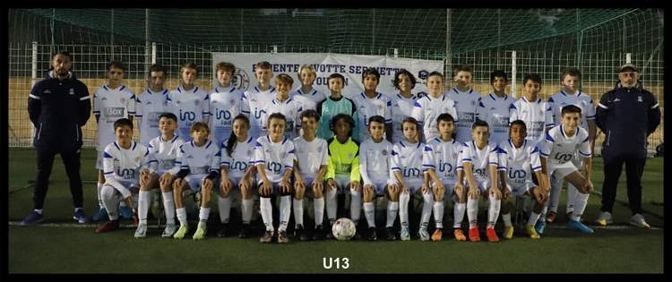 Une équipe de jeunes footballeurs pose avec leurs entraîneurs sur un terrain de sport, devant une banderole.