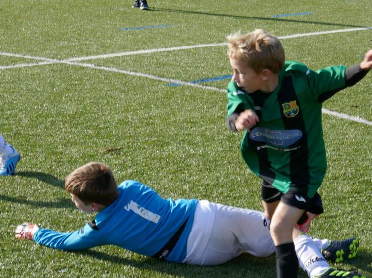 Deux jeunes joueurs de football en pleine action sur un terrain en gazon synthétique.