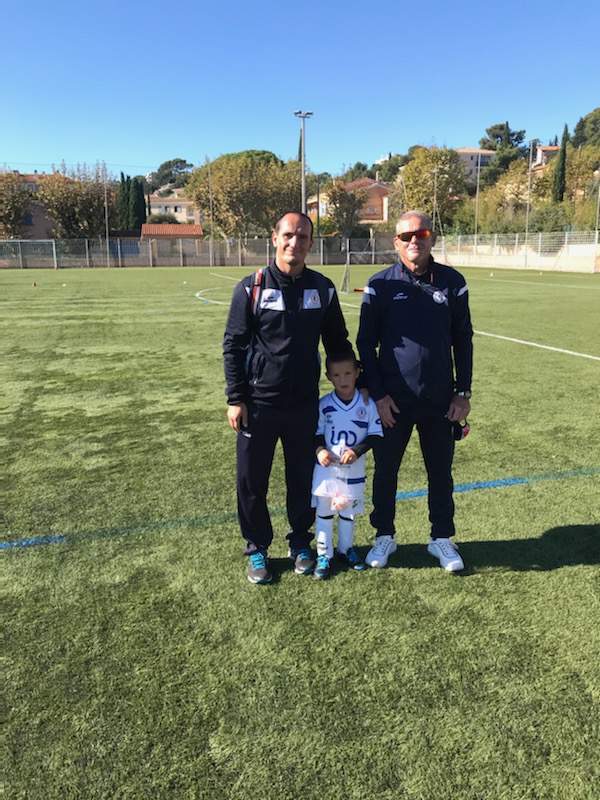 Deux adultes et un jeune enfant posent sur un terrain de football ensoleillé.