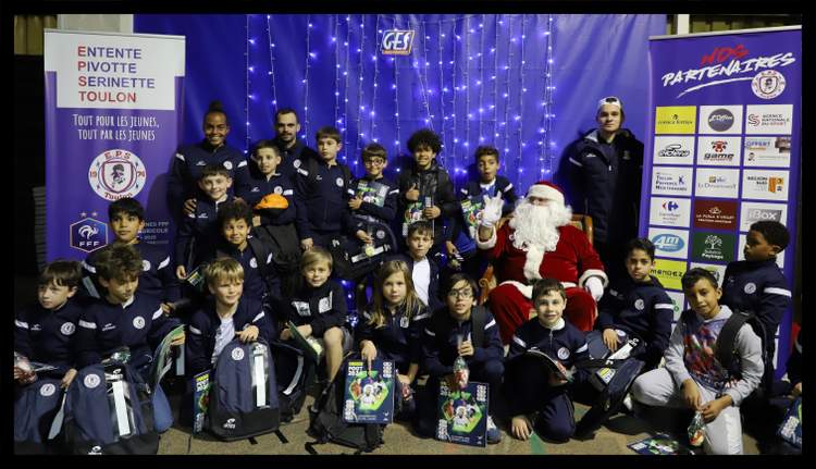 Une équipe de jeunes footballeurs pose avec des adultes et le Père Noël devant des banderoles de sponsors.