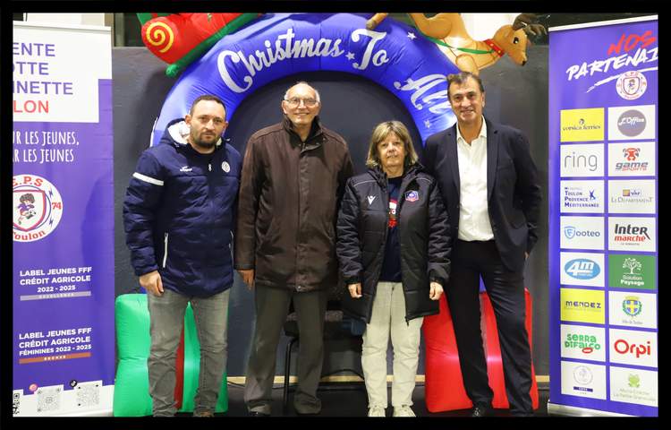 Quatre personnes posent devant une arche gonflable de Noël et des kakémonos de sponsors.