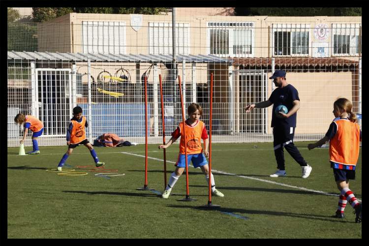 Des jeunes joueurs de football s'entraînent sur un terrain en gazon synthétique avec un entraîneur.