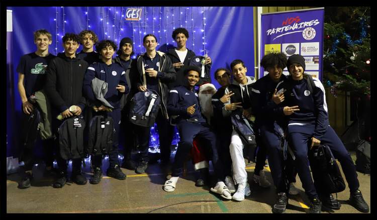 Une équipe de jeunes footballeurs pose avec leurs sacs de sport devant un mur décoré de lumières et un sapin de Noël.