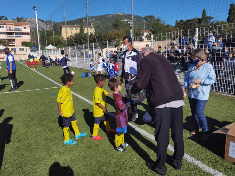 Des jeunes joueurs de football reçoivent des récompenses sur le terrain, sous le regard d'adultes et de spectateurs.