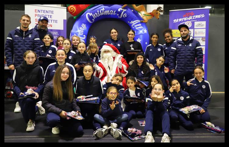 Une équipe de jeunes joueuses de football pose avec le Père Noël et des adultes, devant un décor de Noël et des bannières de partenaires.