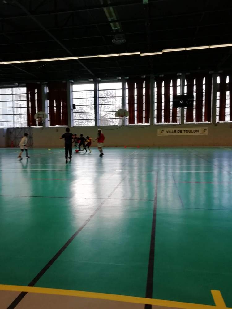 Des jeunes joueurs s'entraînent au football en salle sur un terrain vert.