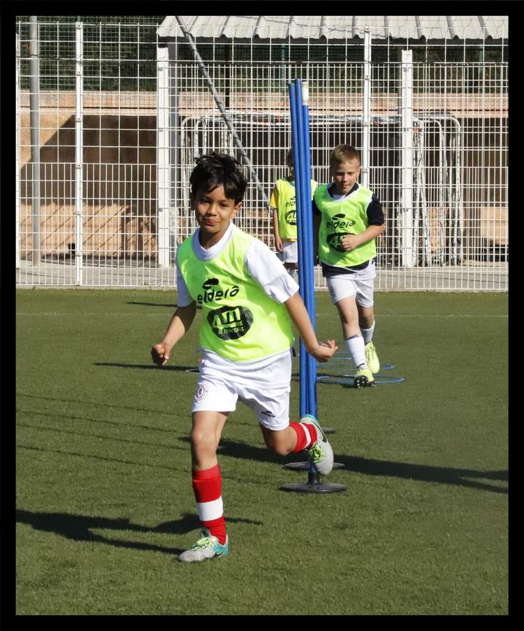 De jeunes footballeurs en chasubles fluorescentes s'entraînent sur un terrain ensoleillé.